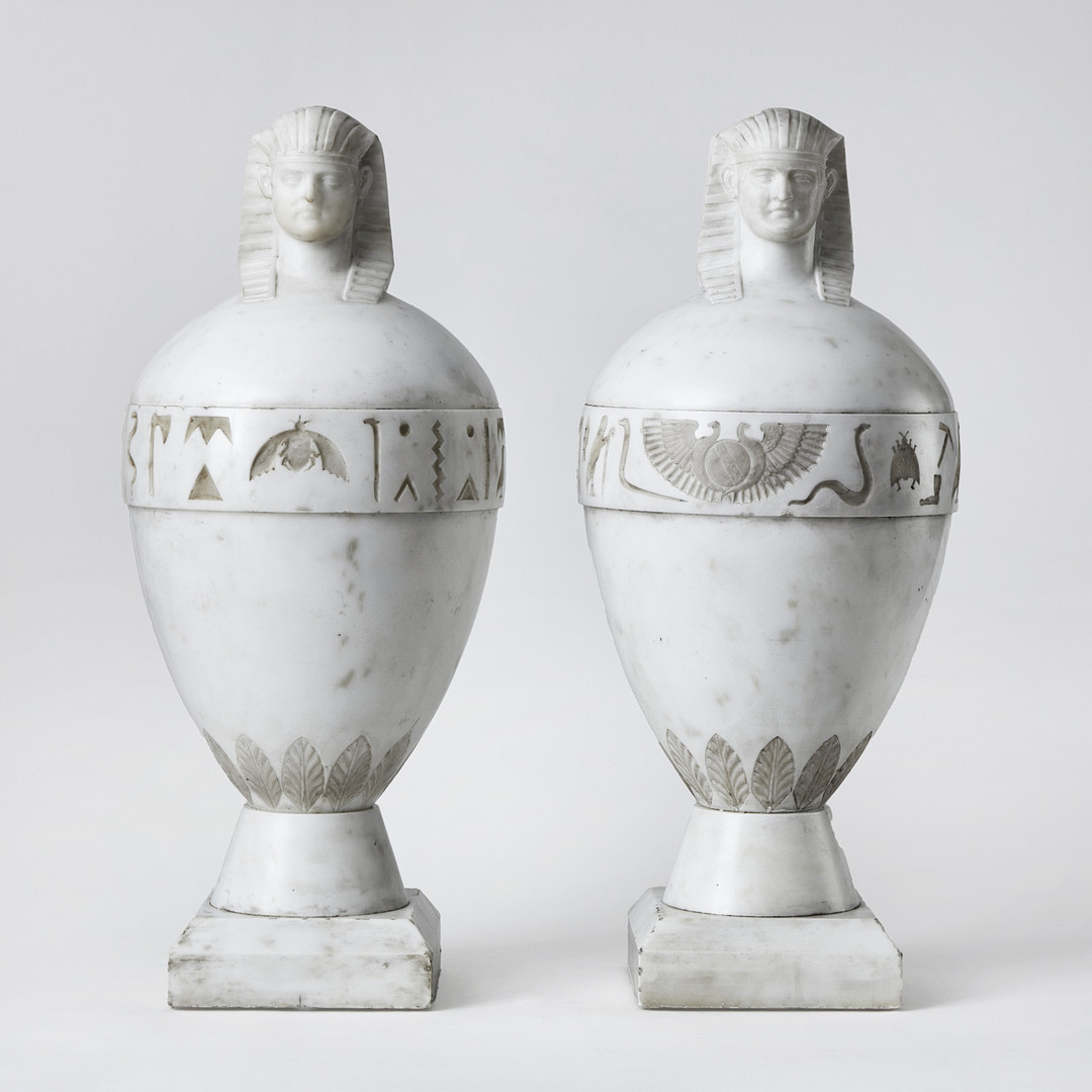 KANOPER RETOUR d'EGYPTE, ett par, Italien 1800-talets första hälft, skulpterad carraramarmor, krönta av dubbelsidiga Antinous-Osiris huvuden.