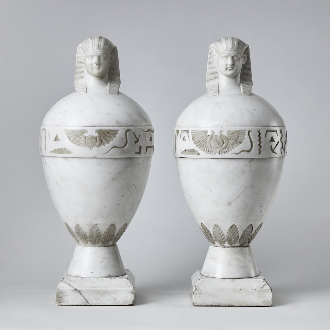 KANOPER RETOUR d'EGYPTE, ett par, Italien 1800-talets första hälft, skulpterad carraramarmor, krönta av dubbelsidiga Antinous-Osiris huvuden.