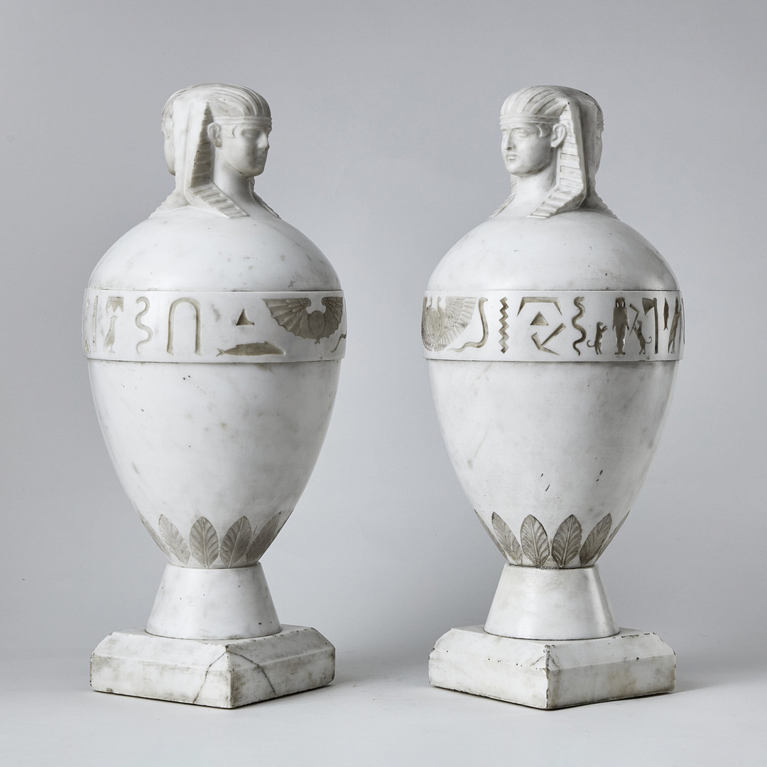 KANOPER RETOUR d'EGYPTE, ett par, Italien 1800-talets första hälft, skulpterad carraramarmor, krönta av dubbelsidiga Antinous-Osiris huvuden.