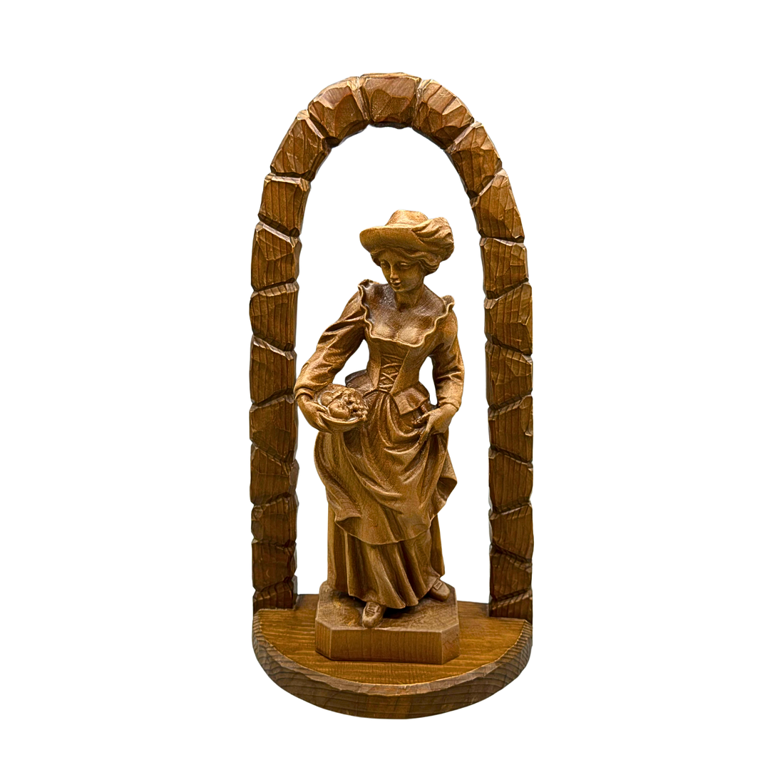HANDGESCHNITZTE HOLZFIGUR EINER FRAU MIT OBSTKORB UND TRACHT UNTER EINEM HOLZBOGEN.