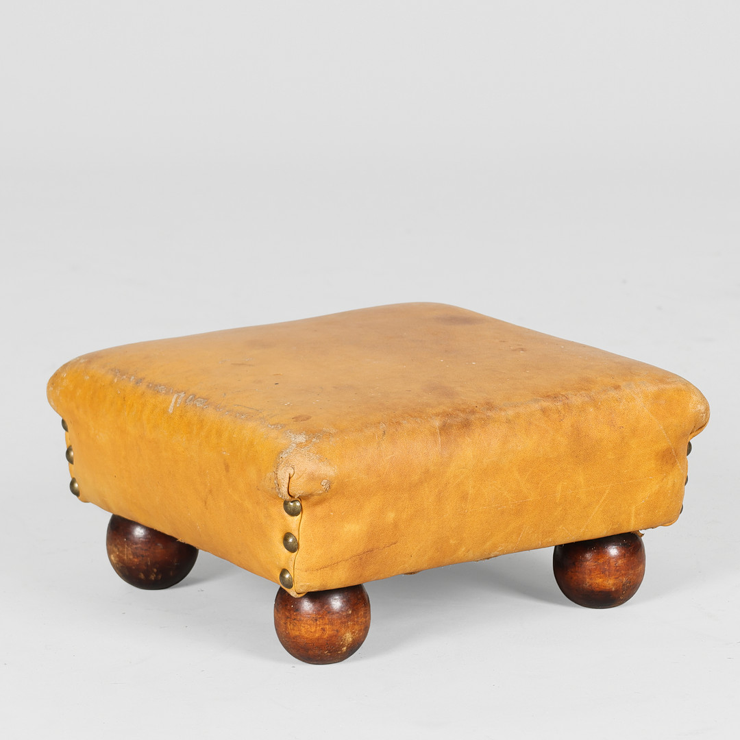 Fodskammel betrukket med patineret skind, fødder af bejdset bøg, 1900-tallets første halvdel.
