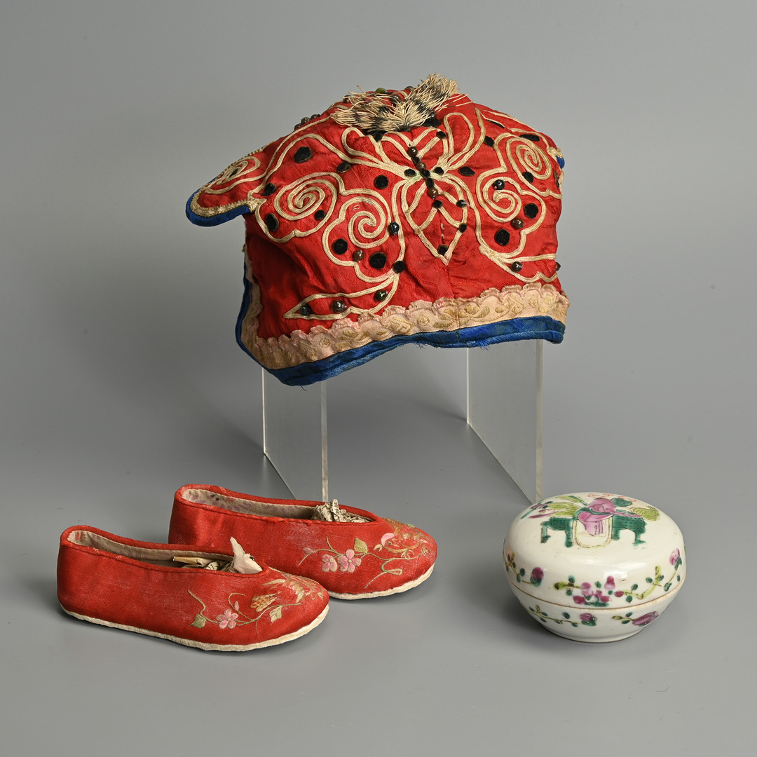 CHINESE SILK EMBROIDERED CHILDREN'S HAT AND SHOES WITH A FAMILLE ROSE PORCELAIN PASTE BOX AND COVER, 19/20TH CENTURY.