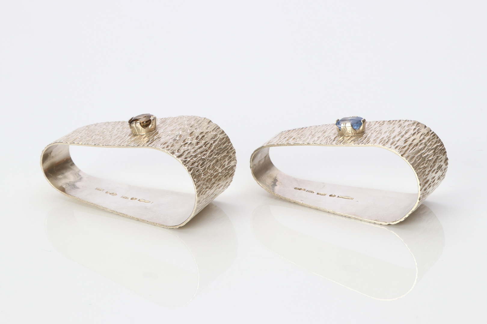 SERVETTRINGAR, TVÅ ST. Sterlingsilver med en safir och en brun zirkon, Sven Seblings juvelateljé, Göteborg 1983-84, totalvikt ca 60,3 gram.
