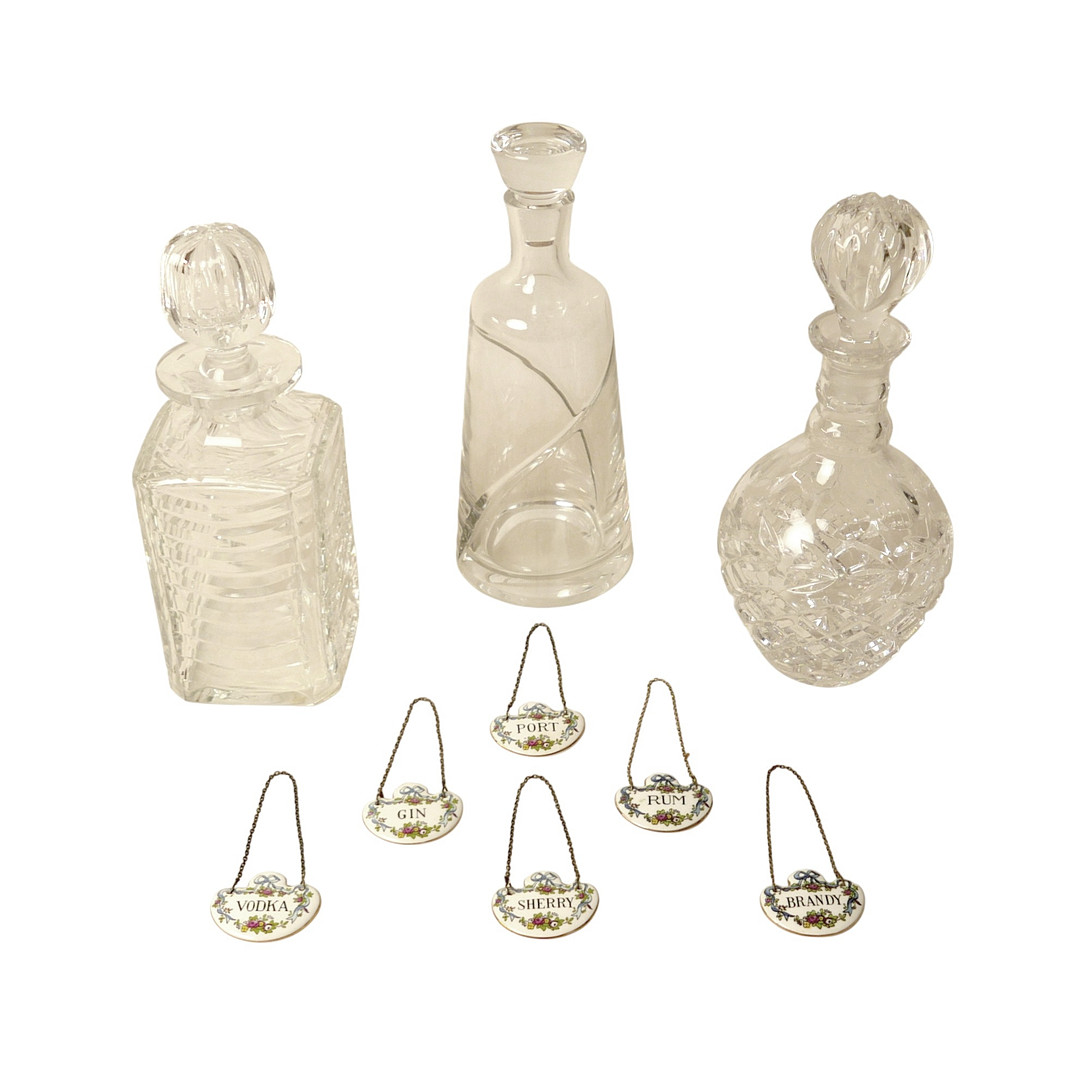 THREE GLASS DECANTERS AND SIX CERAMIC SPIRIT LABELS.