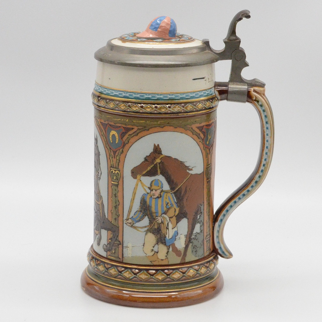 VILLEROY & BOCH METTLACH, KERAMIKKRUG; ZINNDECKEL MIT WIDMUNG AUS 1892, 3X JOCKEY MIT PFERD MOTIV, MODELL 1733, RELIEFIERT UND MIT GOLDMALEREI, DEUTSCHLAND.