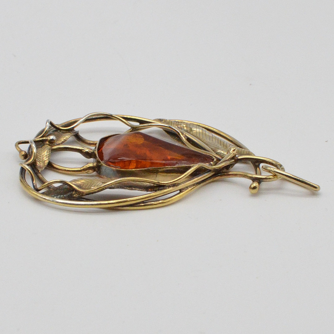 JUGENDSTIL COLLIERANHÄNGER MIT EINEM BERNSTEIN, DURCHBROCHENE FASSUNG AUS VERGOLDETEM STERLINGSILBER, BERNSTEIN MIT BLATTEINSCHLÜSSE, HANDGEMACHT, UNLESERLICH PUNZIERT, FRÜHES 20. JAHRHUNDERT.