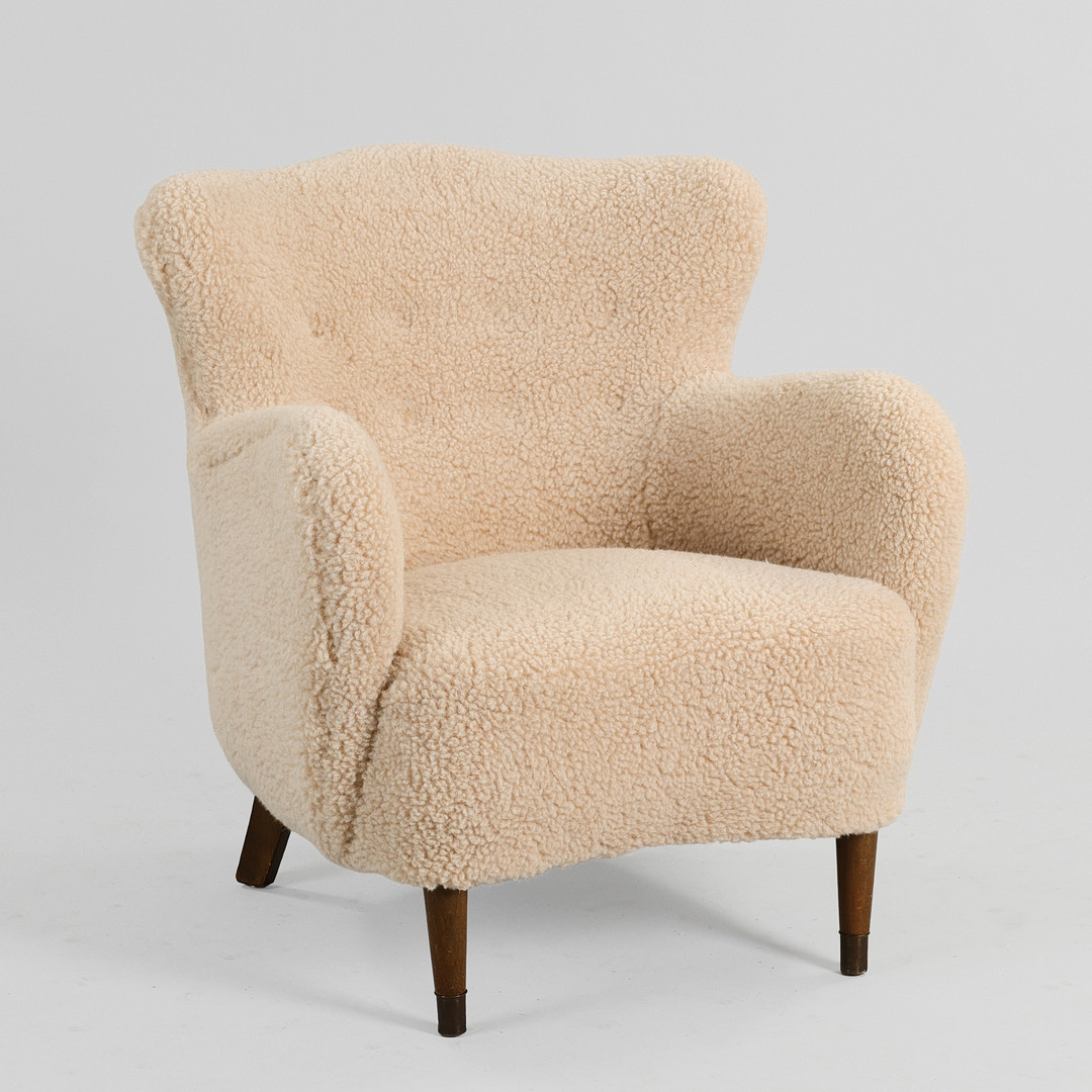 DANSK MØBELDESIGN. Overpolstret lænestol betrukket med lyst imiteret lammeskind, ben med messingsko, 1900-tallets midte.