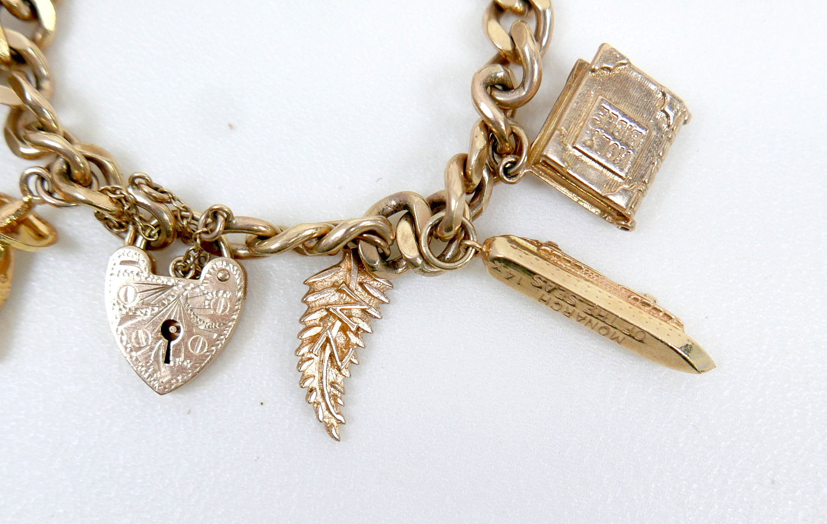 A 9CT GOLD CHARM BRACELET, FLAT CURB, WITH ASSORTED 9CT AND 14CT GOLD CHARMS.