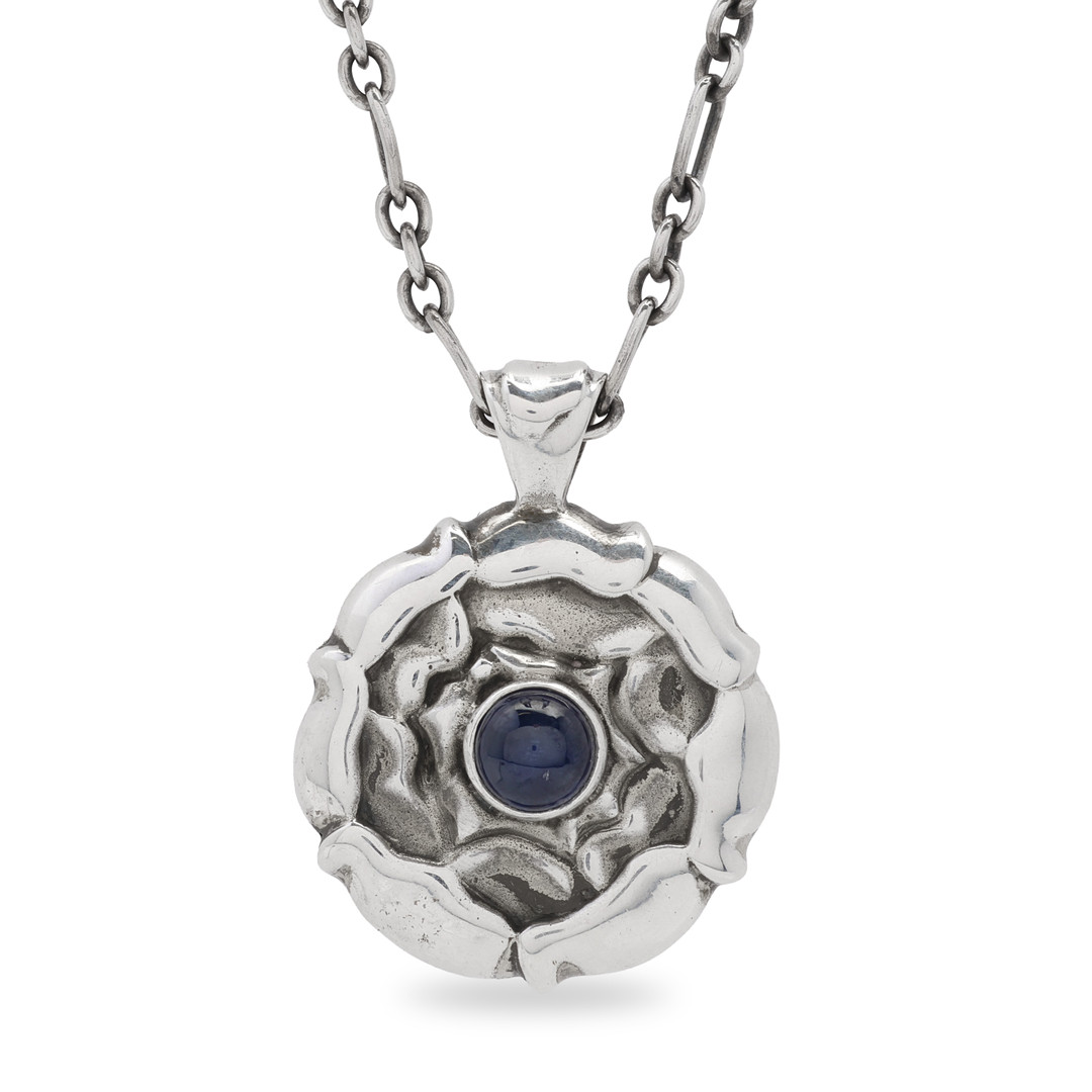 Ole Kortzau for Georg Jensen. Månedssmykke af sterlingsølv i form af blomsterformet vedhæng med blå sten. Danmark.