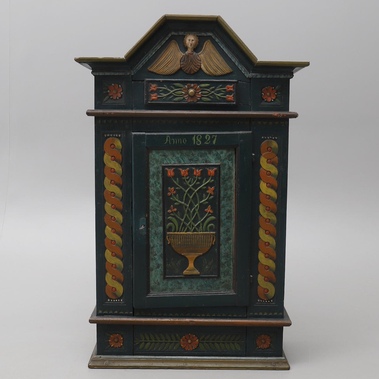 ENGELSCHRANK, bemalt mit Reliefschnitt, der einen Blumentopf, Fleurons, ein Bandgeflecht und einen krönenden Engel darstellt.