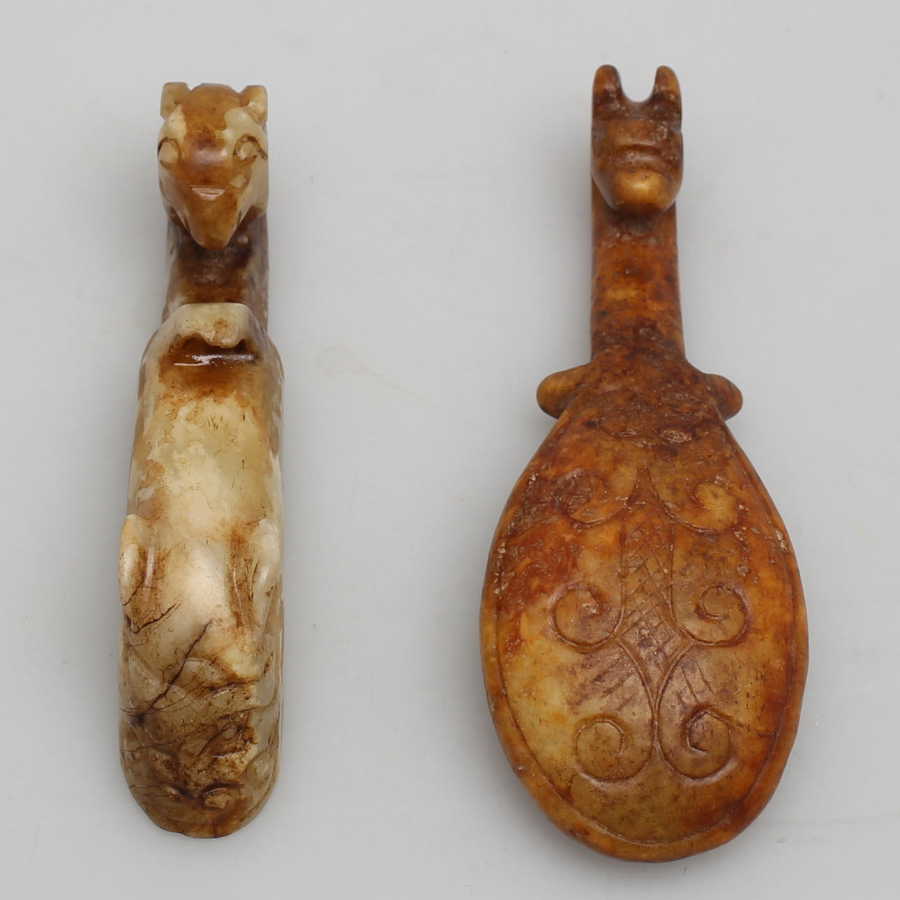 BÄLTESSPÄNNE. 2 st. Stenarbeten. Troligen jade. Dekor av djurhuvuden.