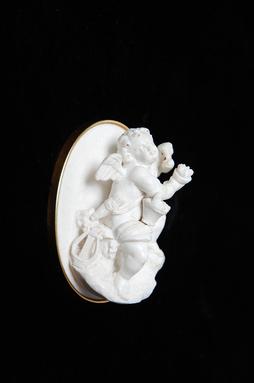 BROSCH, 18 K guld, "Putto i hög relief " stämplad Gustaf Möllenborg, Stockholm oglaserat porslin.