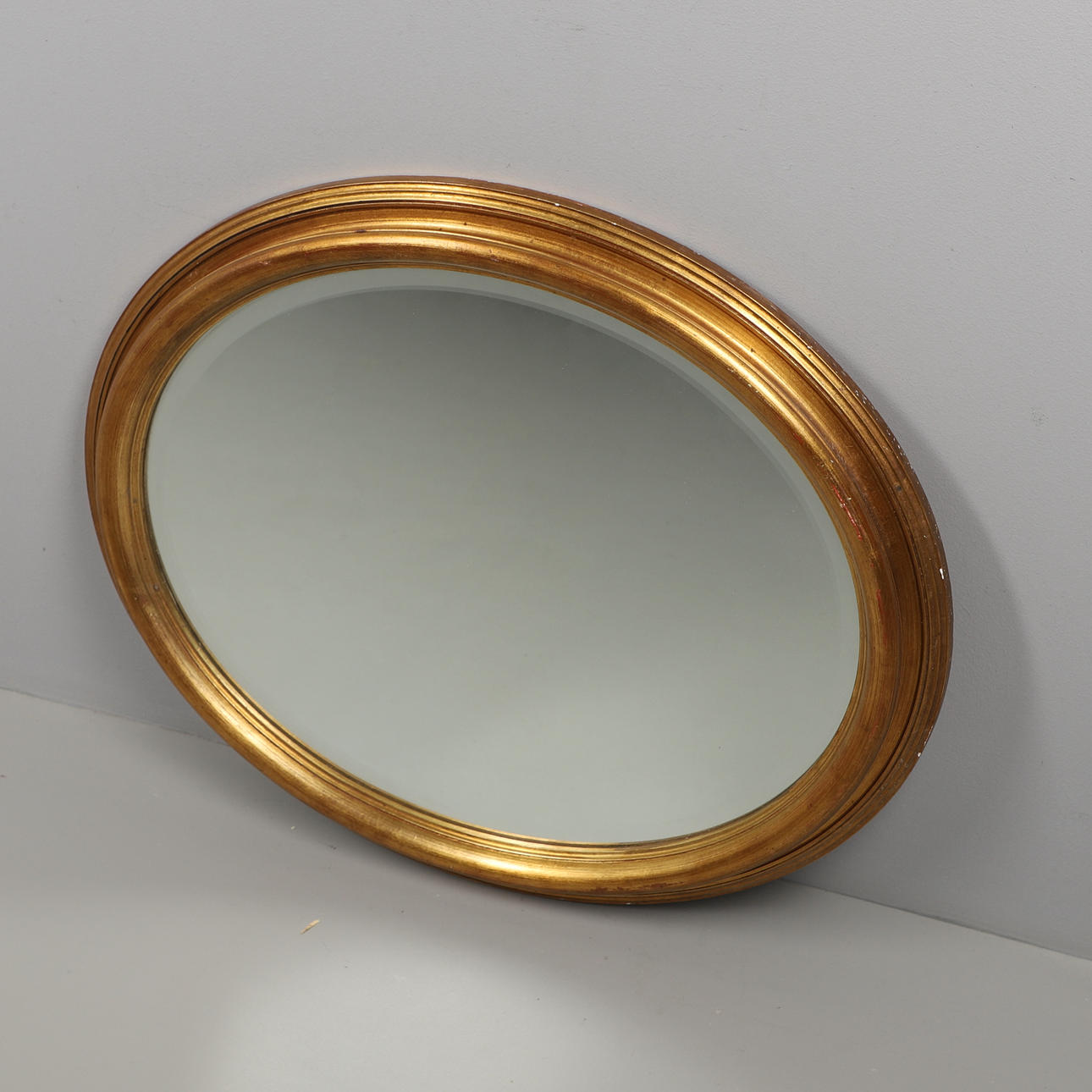 AN OVAL GILT FRAMED MIRROR.
