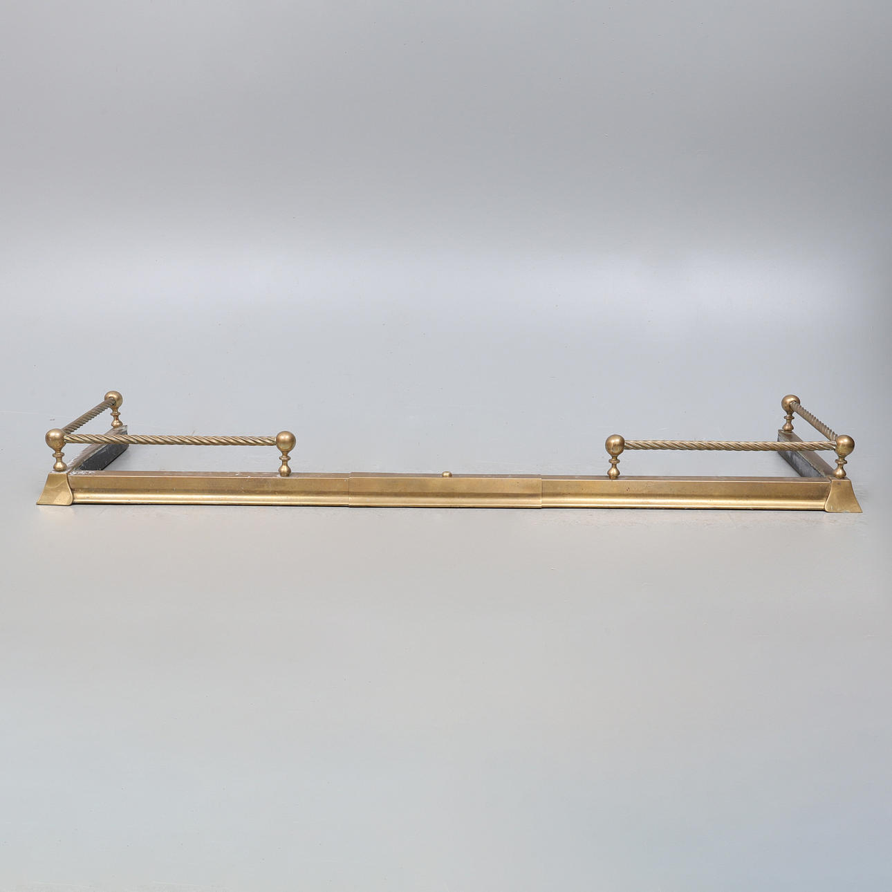 AN EDWARDIAN BRASS FENDER, ORIGINALLY ADJUSTABLE, NOW FIXED.
