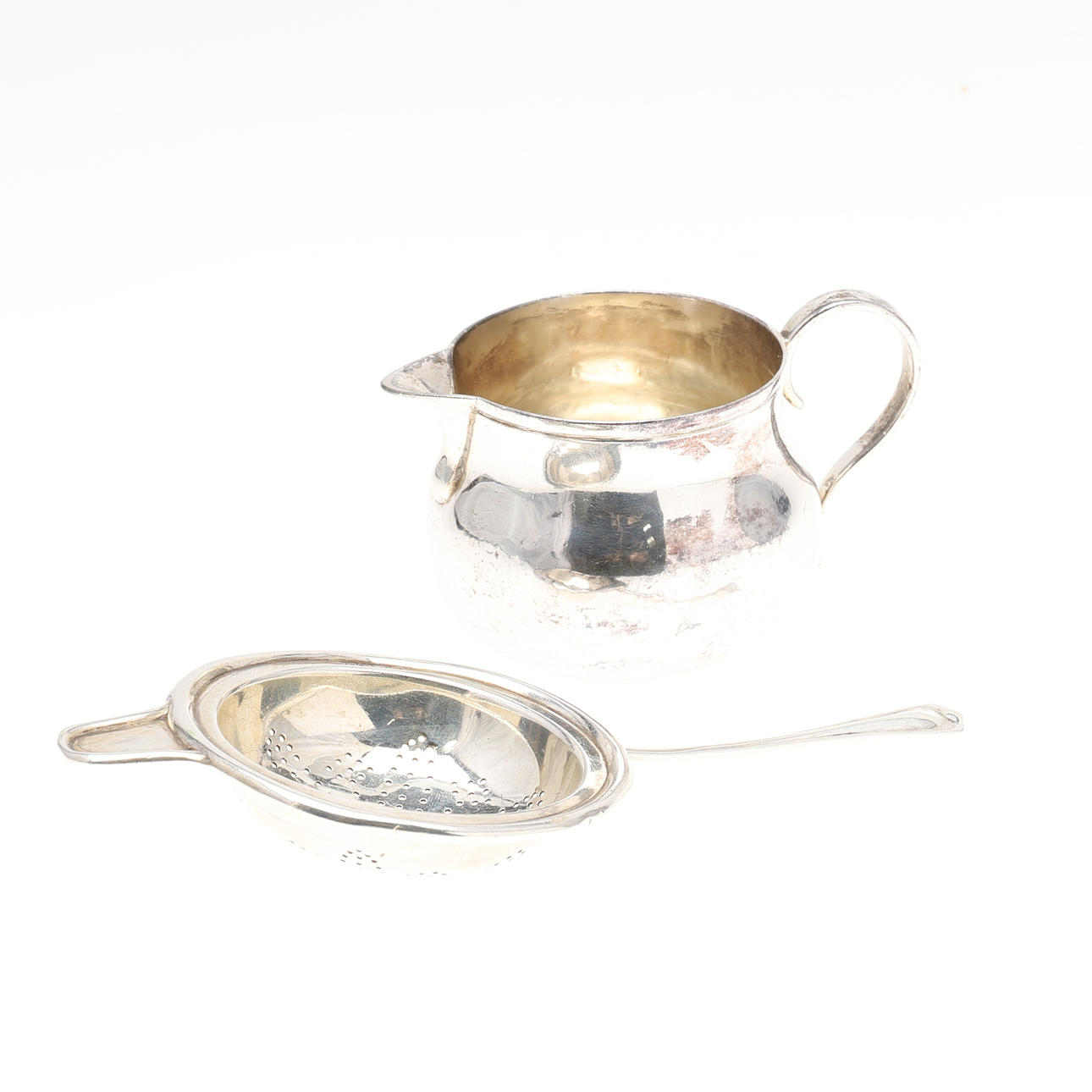 A VICTORIAN SILVER JUG AND AN EDWARDIAN TEA STRAINER.