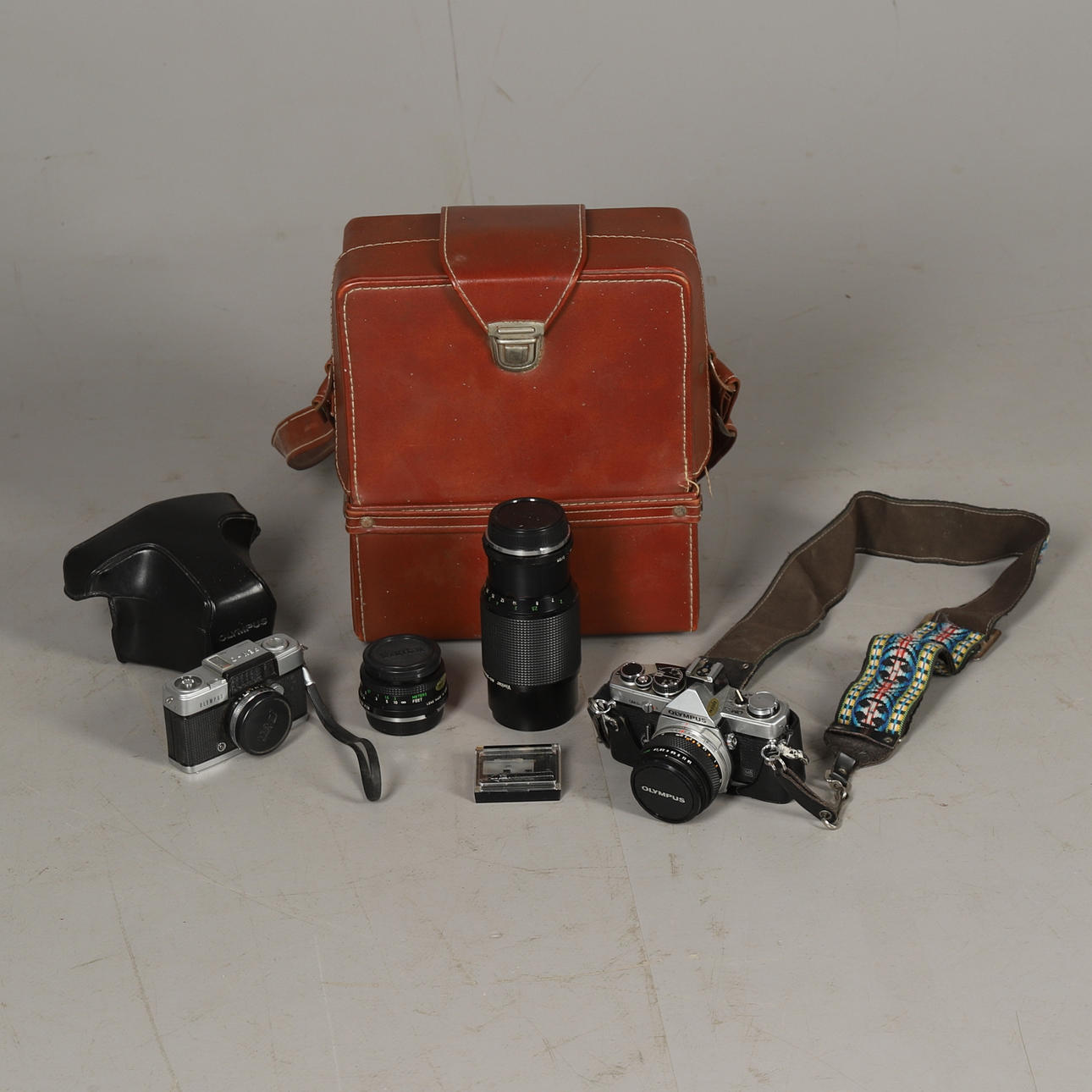 EINE OLYMPUS OM-2 KAMERA IN HELLBRAUNEM LEDERTASCHE, EINE MENGE OBJEKTIVE UND EINE WEITERE OLYMPUS KAMERA.