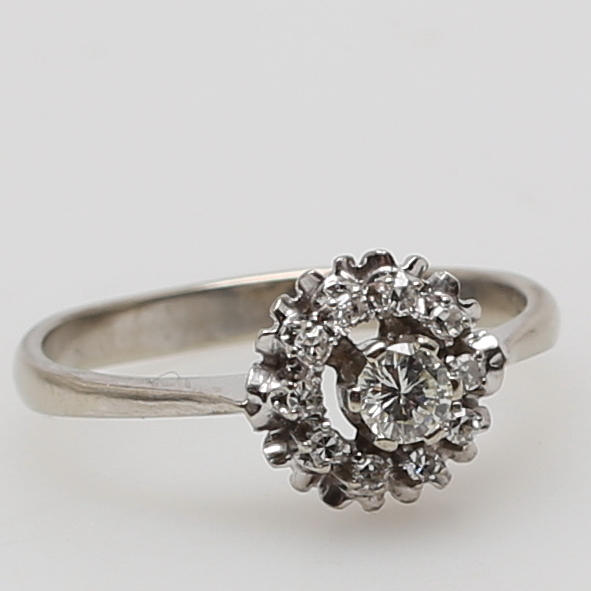 RING i 18K vitguld besatt med diamant om ca 0,20 carat samt krans av tio mindre diamanter, enligt gravyr 0,26 carat.