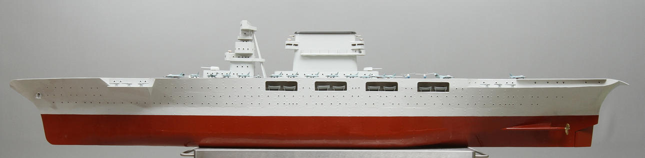 FARTYGSMODELL, hangarfartyg med inbyggd el. Grå och rödlackerad plåt. Troligen amerikansk förebild. Ett tjugotal flygplansmodeller medföljer. . Byggare: Erik Mogensen.