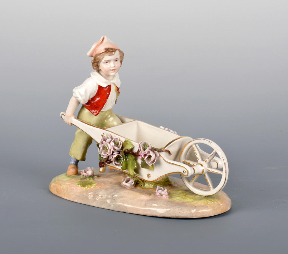 PLAUE SCHIERHOLZ. Härlig porslinsfigur; pojke med blomma-dekorerad handvagn.