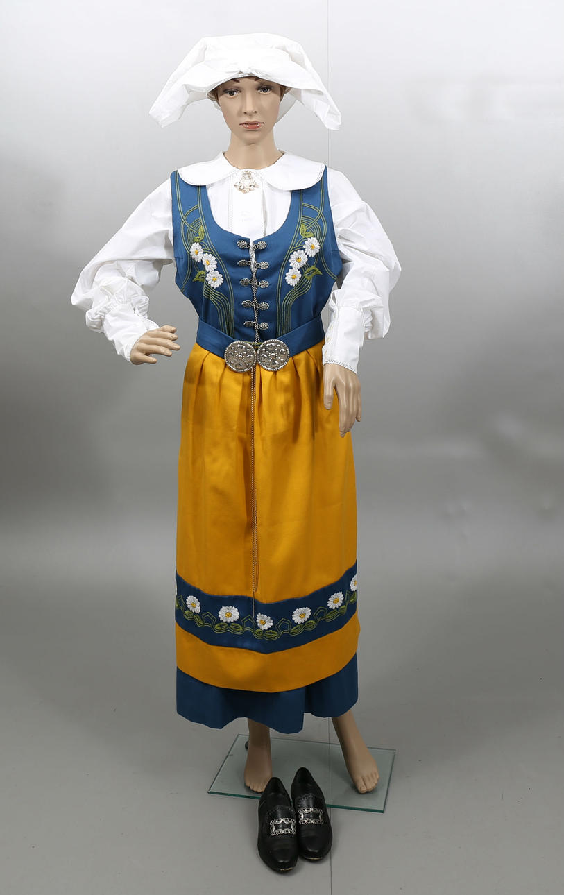 FOLKDRÄKT, Sverigedräkten, bestående av blus, klänning, förkläde, skärp, huvudbonad, och skor, 1993.