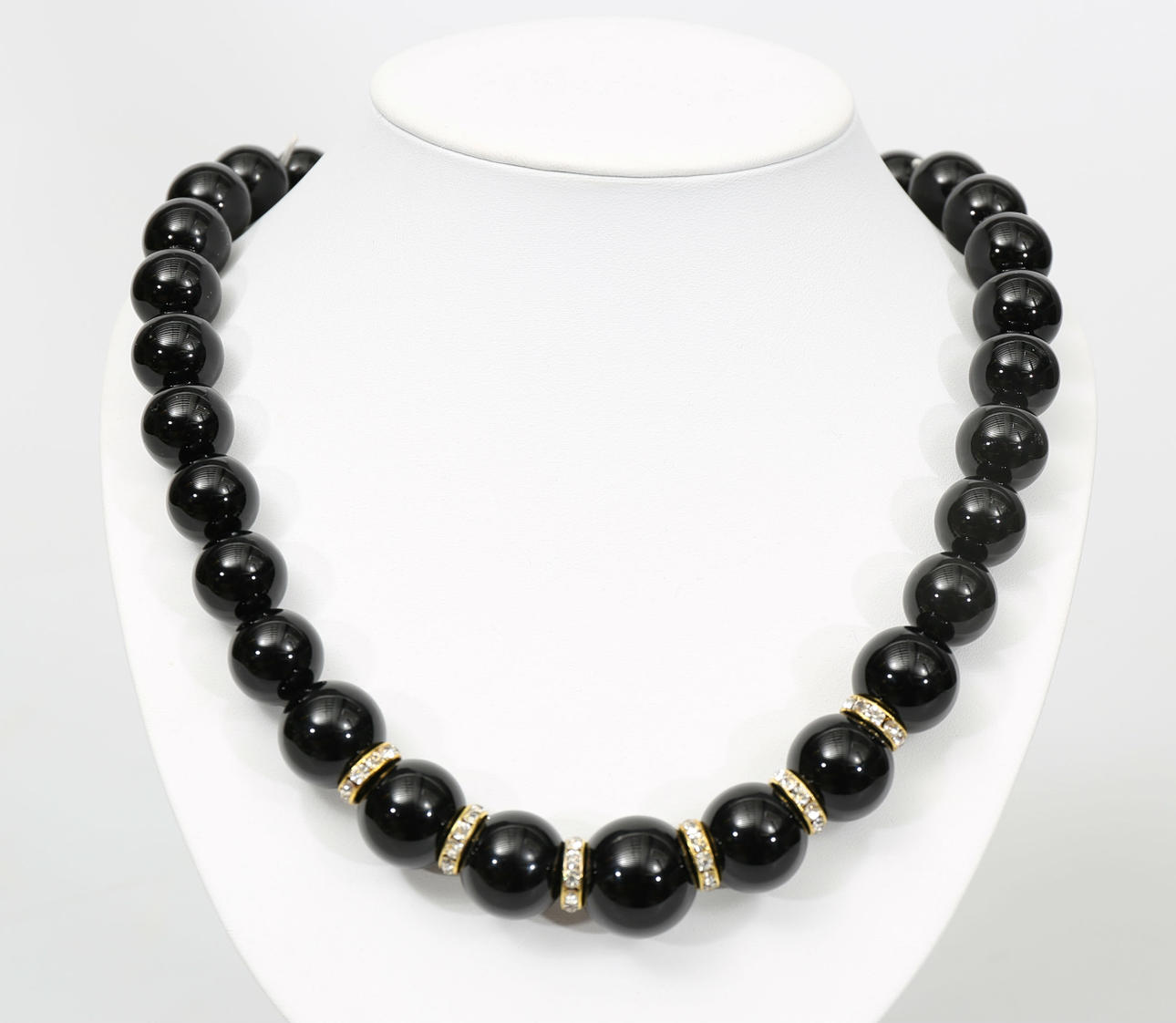 COLLIER, svarta polerade stenkulor och dekorerad med ringar i gulmetall och vita stenar, 2000-tal.