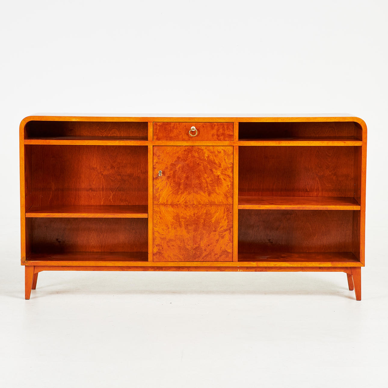 A bookcase, circa 1940's, veneered with birch, rounded corners, cabinet section, shelving, drawer and shelves.
