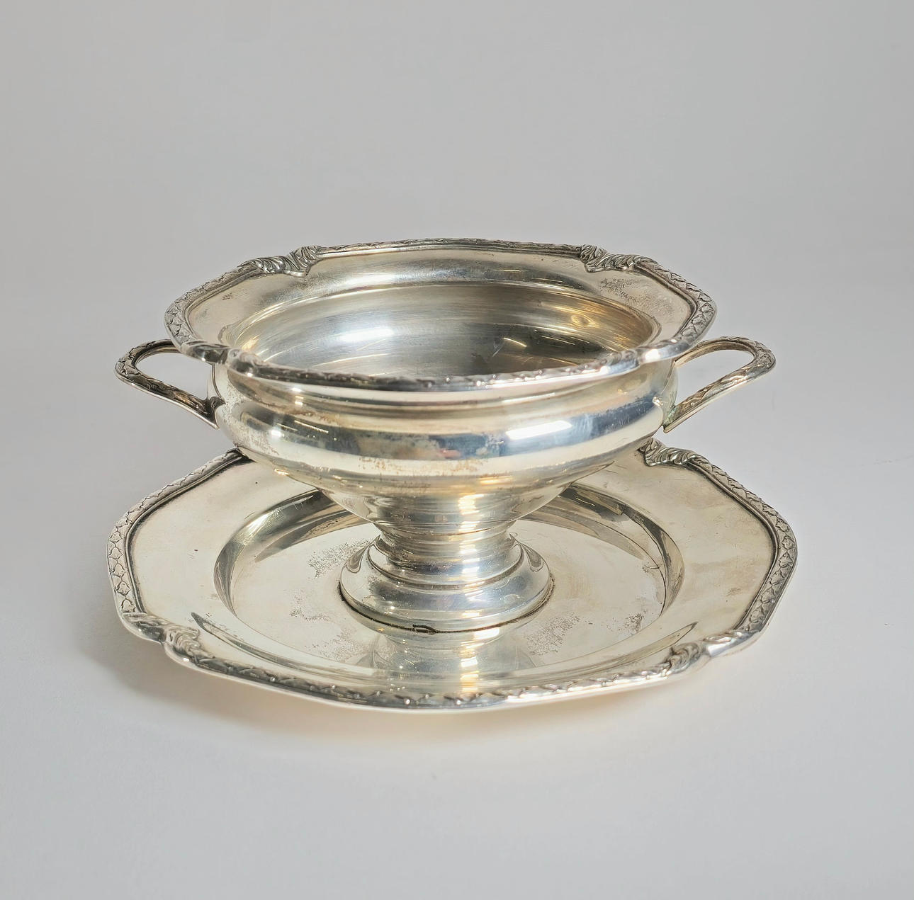 PUNCHED SILVER SAUCE DISH WITH BOTTOM PLATE, DOUBLE HANDLE AND VEGETABLE BORDER.