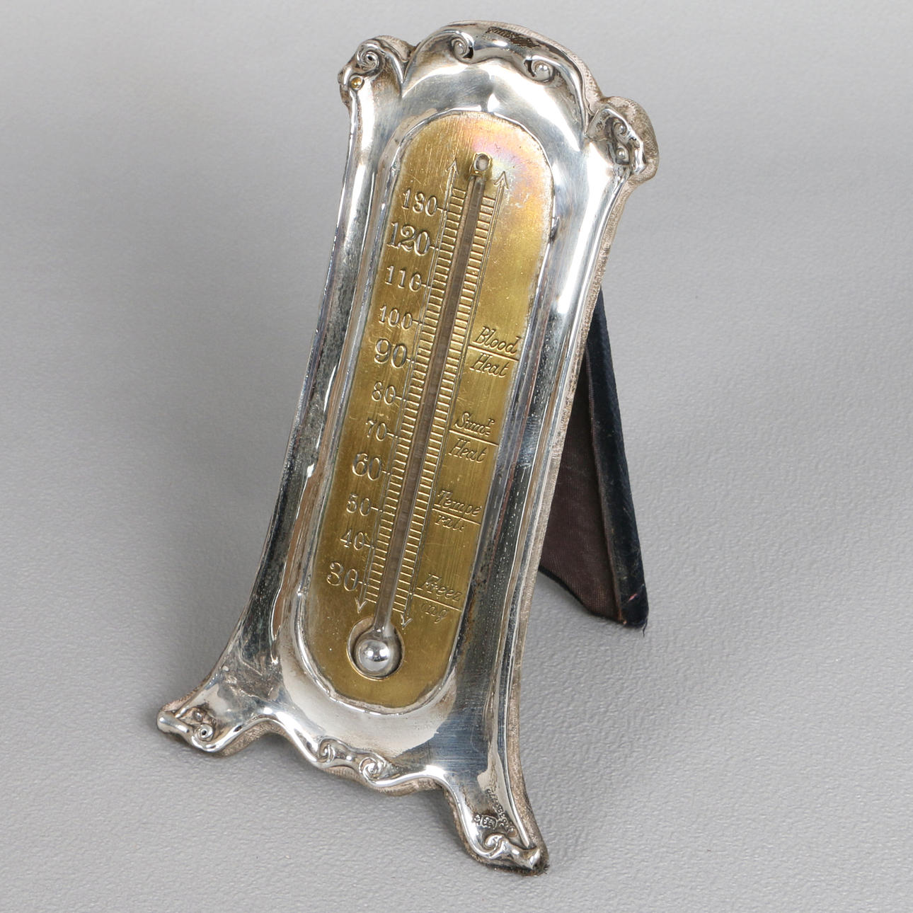AN ART NOUVEAU SILVER-MOUNTED BRASS TABLE THERMOMETER.