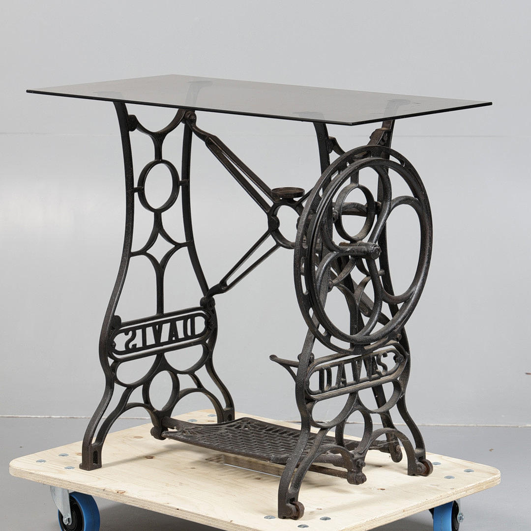 A DAVIS CAST IRON TREADLE SEWING MACHINE TABLE WITH GLASS TOP.