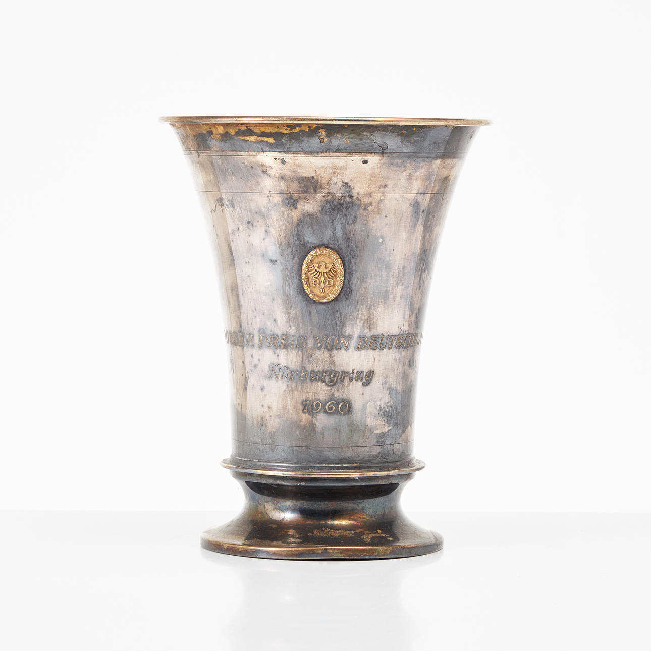 Ein silberner Becher, Firma Hemmerle München, eingravierter Text „Großer Preis von Deutschland Nürburgring 1960" und angebrachtes Emblem.