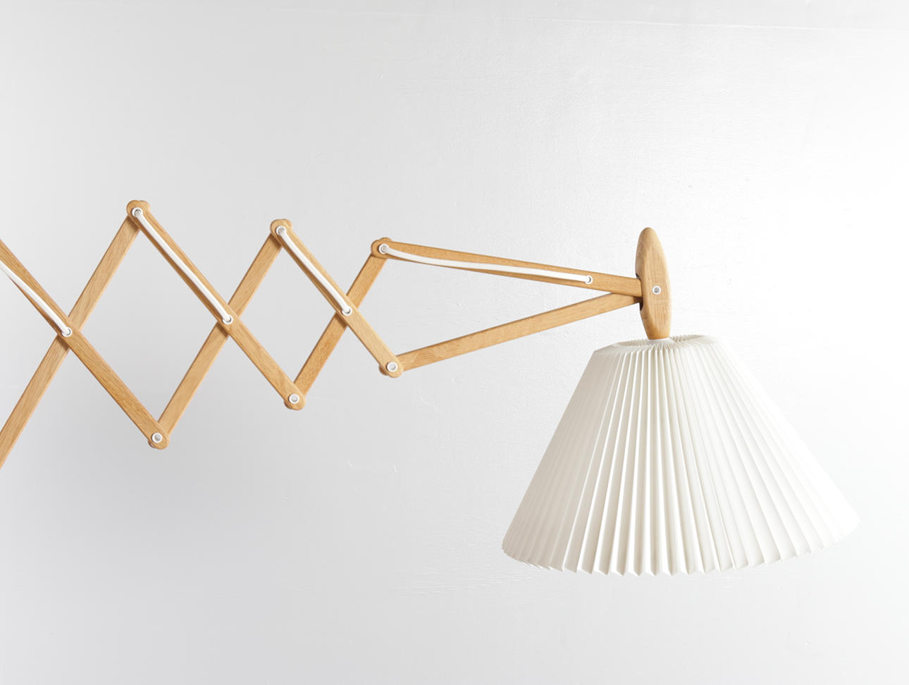 ERIK HANSEN. Wall mounted scissor lamp made of solid oak, mounted with pleated screen. Manufactured at Le Klint, model '322/34'. Designed by Erik Hansen in 1952.