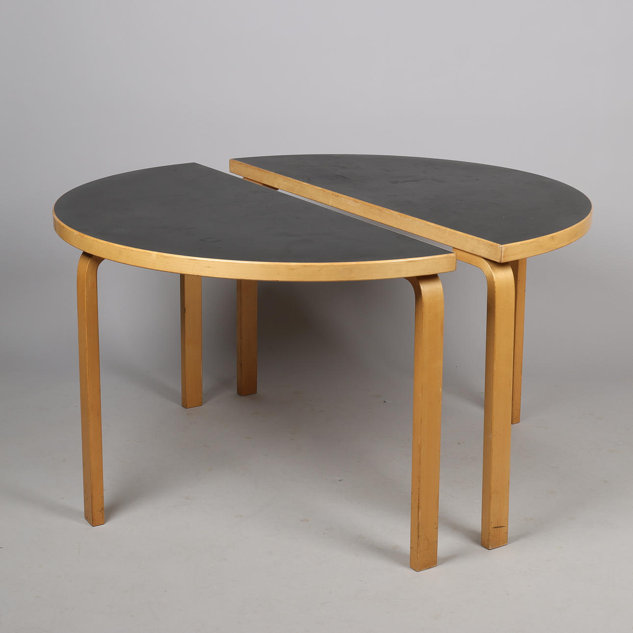 ALVAR AALTO (1898-1976). Round table/ a pair of semi-round tables, model 95, moulded birch and black laminate, Artek, Finland (2).