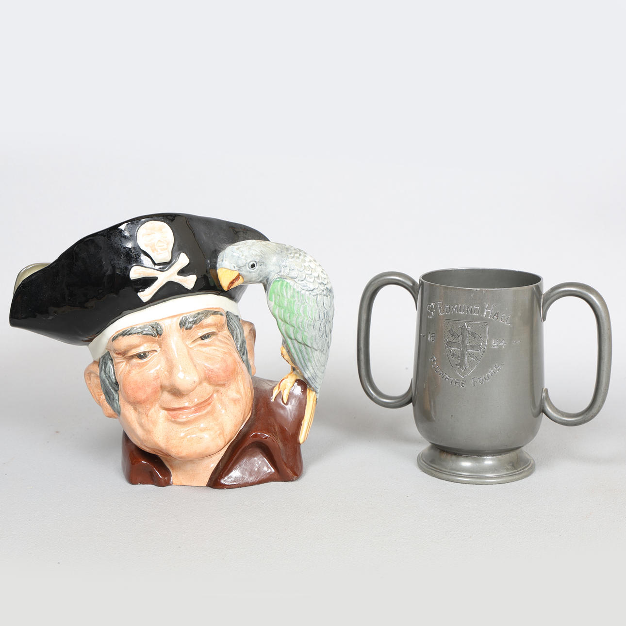 A 'LONG JOHN SILVER' TOBY JUG & A PEWTER TWIN-HANDLED CUP (2).