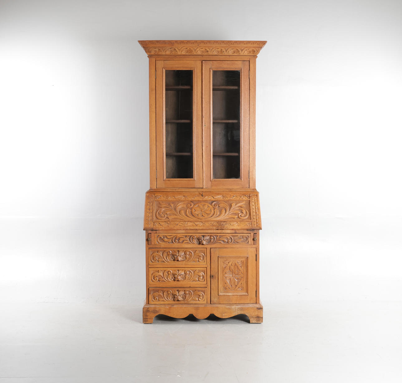 Two-piece chatol of carved oak, front with upper part with doors with glass behind which shelves, including writing flap, drawers and door, 19/20. yay.