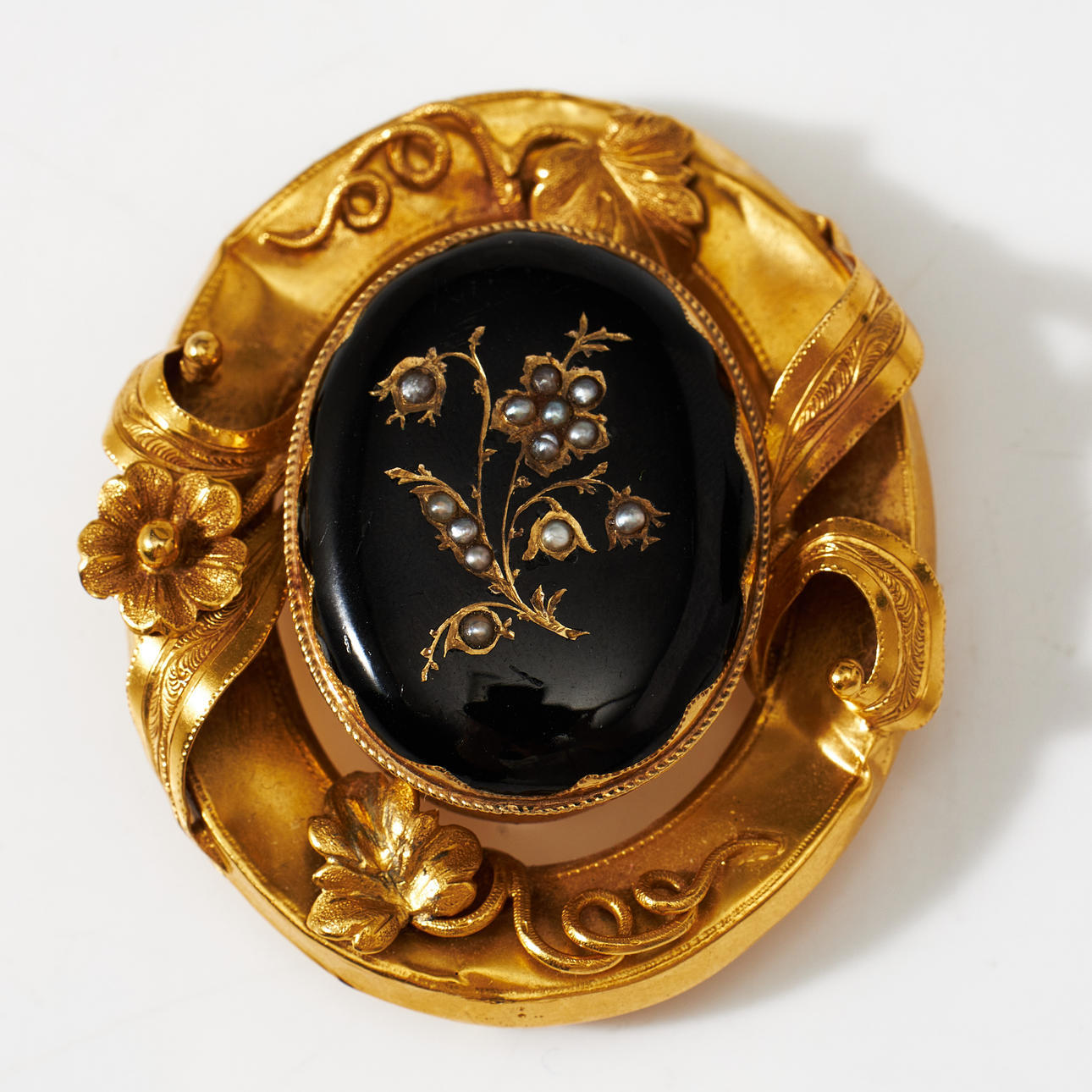 BROOCH, 18k gold, frame with flower and leaf decoration, openable middle part with hide and black enamel and decor with oriental beads in a floral motif, later part of the 19th century, stamped CH and 18K.