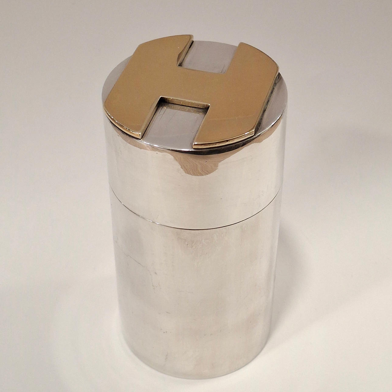 HERMES. „H“ desktop lighter i sølv og guld alpaca.