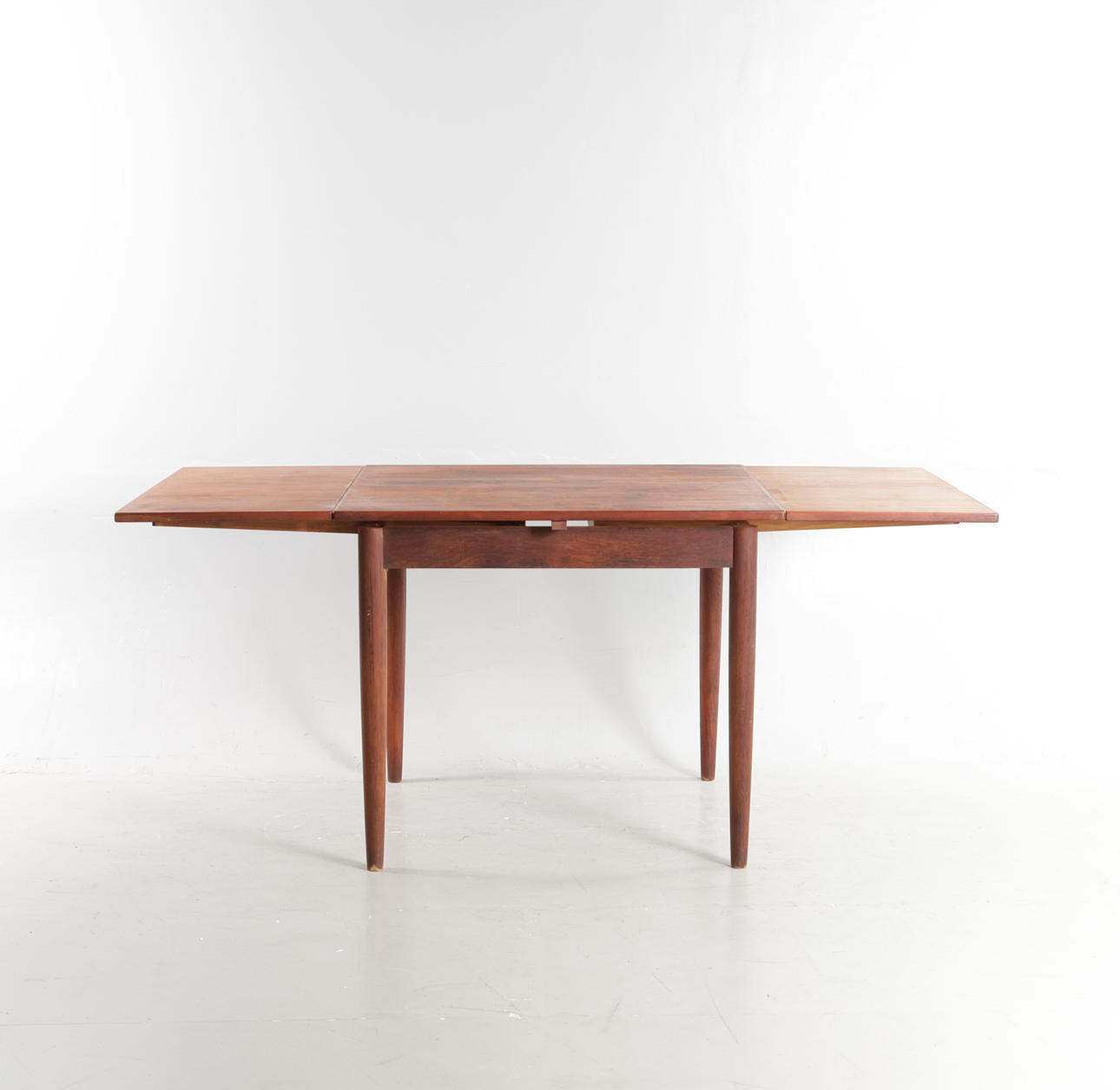 DANSK MØBELDESIGN. Dining table made of teak, square plate with Dutch extraction, round tapered legs. Denmark, 1960s.