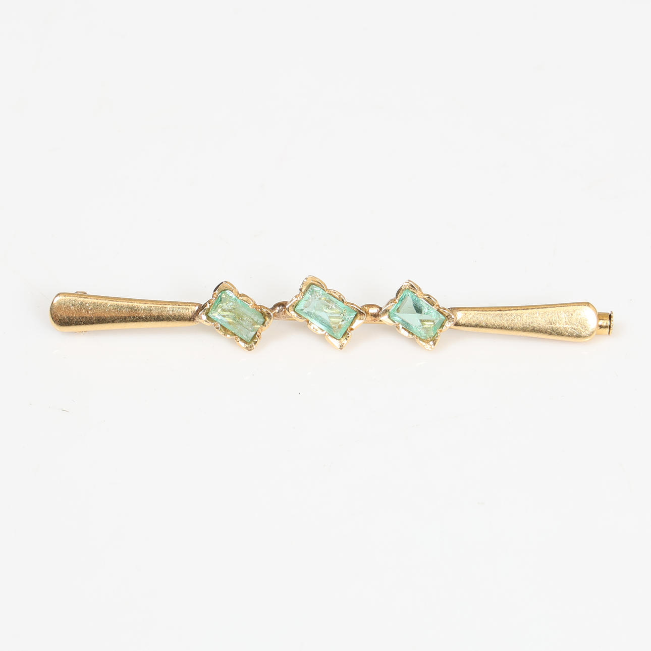 A YELLOW METAL EMERALD SET BAR BROOCH.