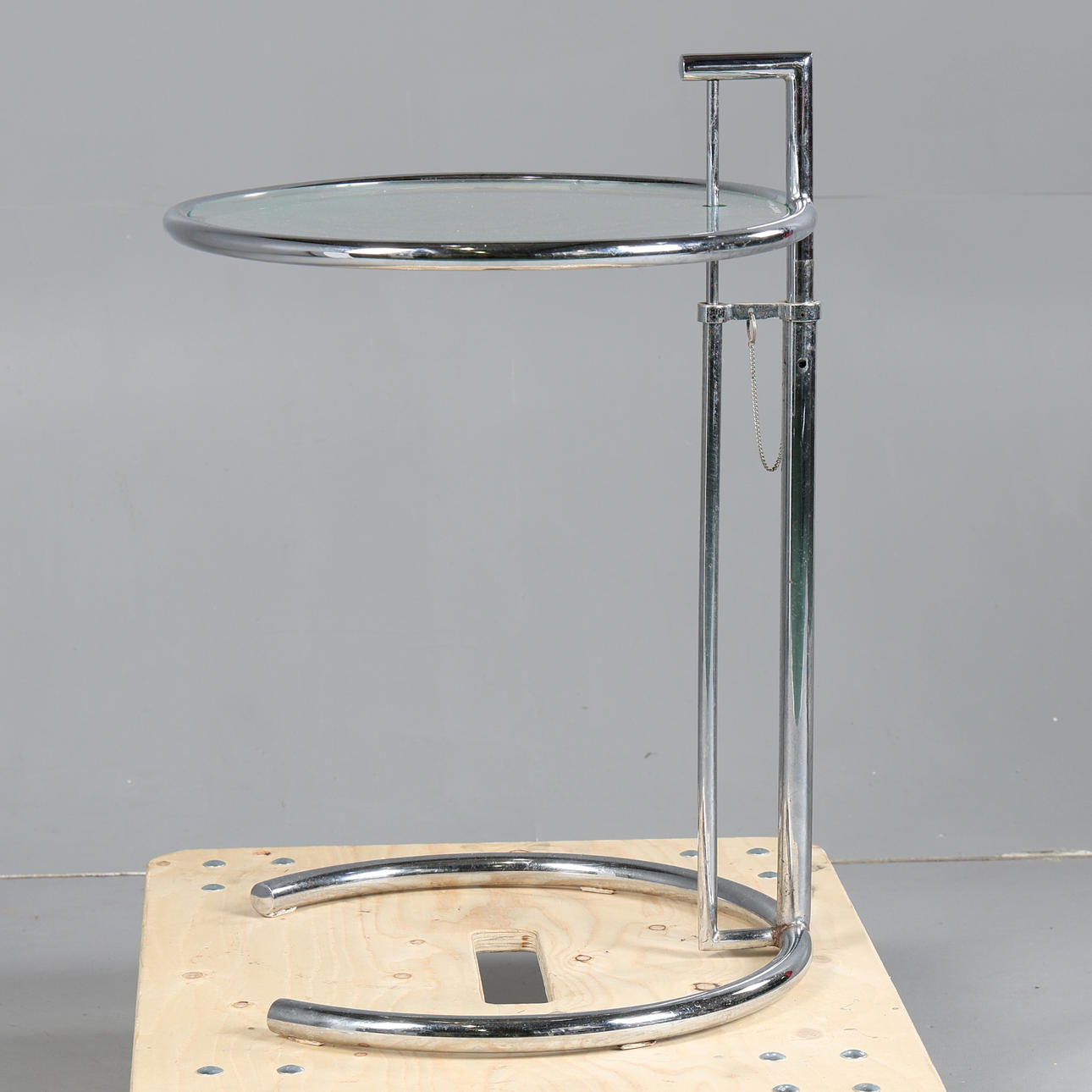 AN ADJUSTABLE CHROME AND GLASS SIDE TABLE.