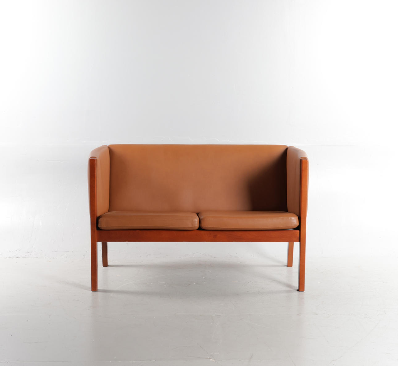HANS J WEGNER. Freestanding two-person sofa with solid teak-stained beech frame, upholstered in cognac colored aniline leather. Designed in 1985. Manufactured and marked at Getama, model “GE 285".