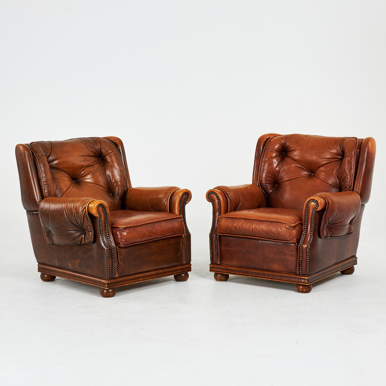 ARMCHAIRS. 1 pair, leather, solid padded frame with deep sewn buttons, beaded nails, wooden ball feet.
