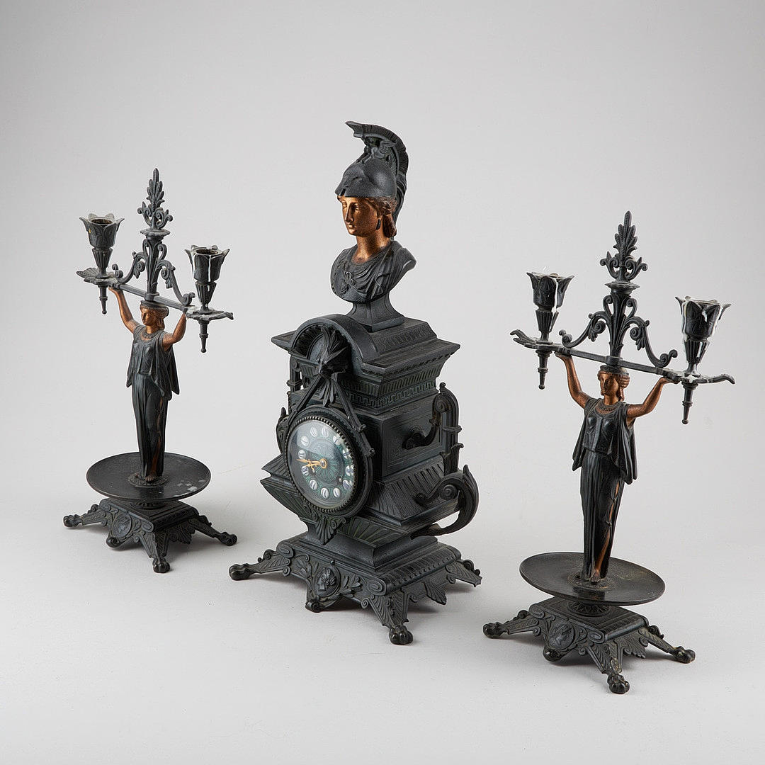 A late 19th century iron Middle European table clock and two candlesticks.