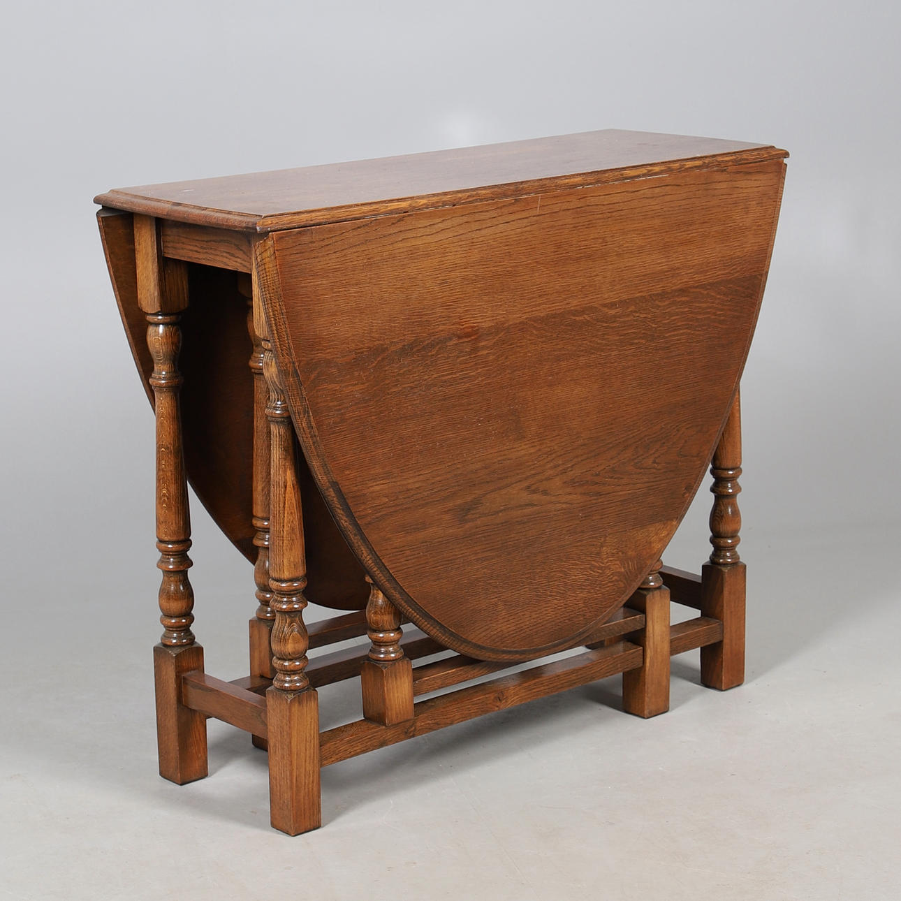 AN OAK DROP LEAF TABLE ON TURNED SUPPORTS.