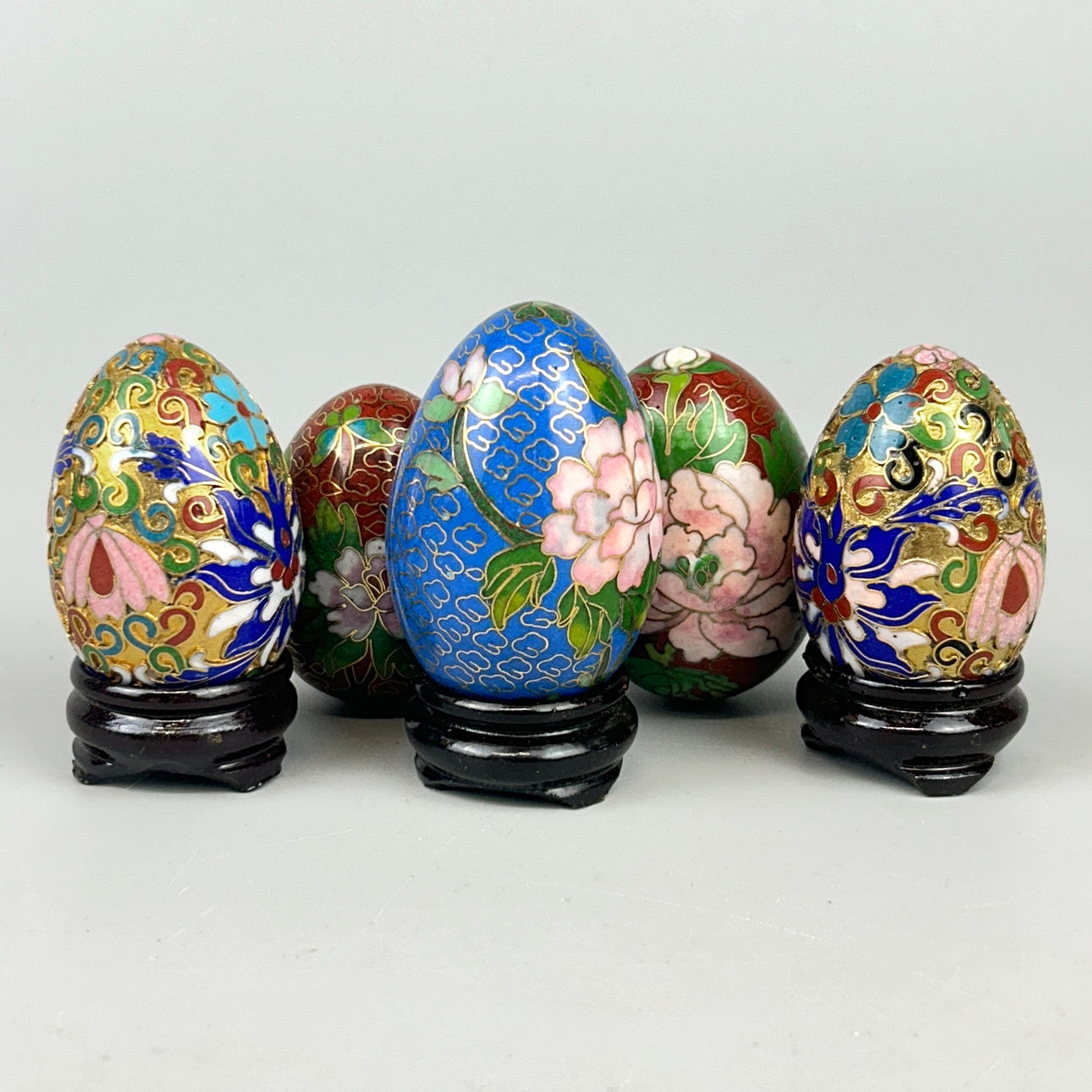 FIVE CLOISONNE EGGS WITH THREE WOODEN STANDS.