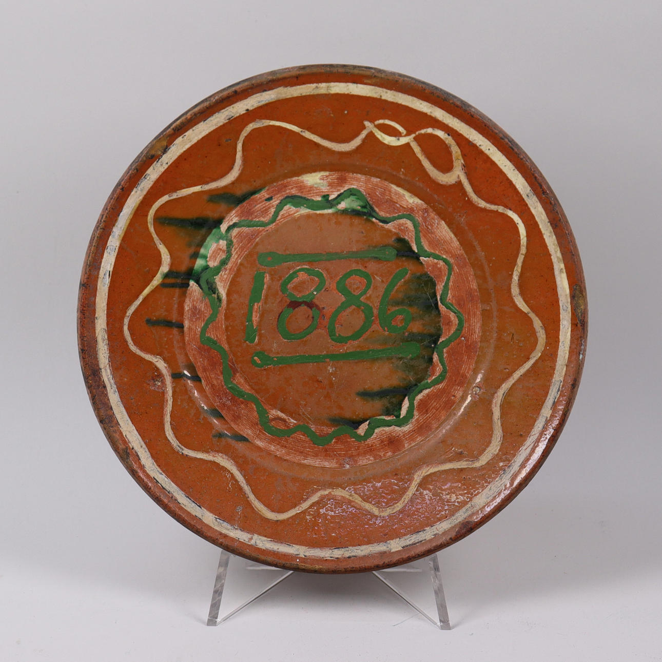 A plate/saucer, almoge, partly glazed earthenware, dated 1886.
