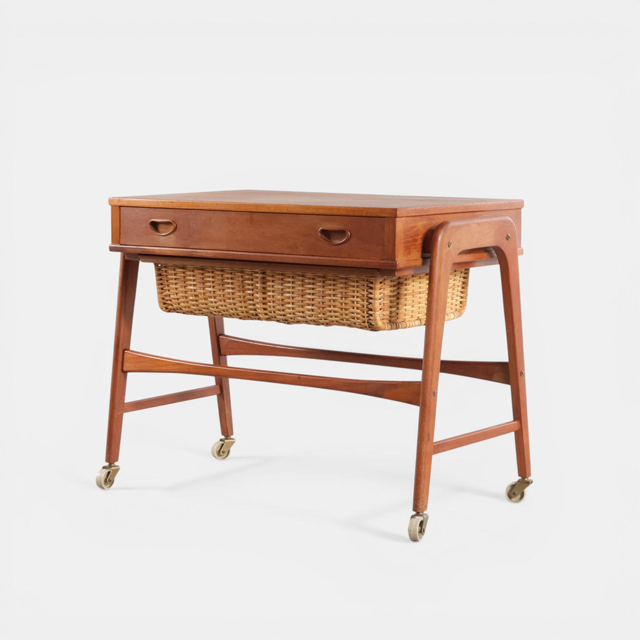 Freestanding teak sewing table, front with compartmentalized drawer, including wicker basket, mounted on wheels. Denmark, 1960s.