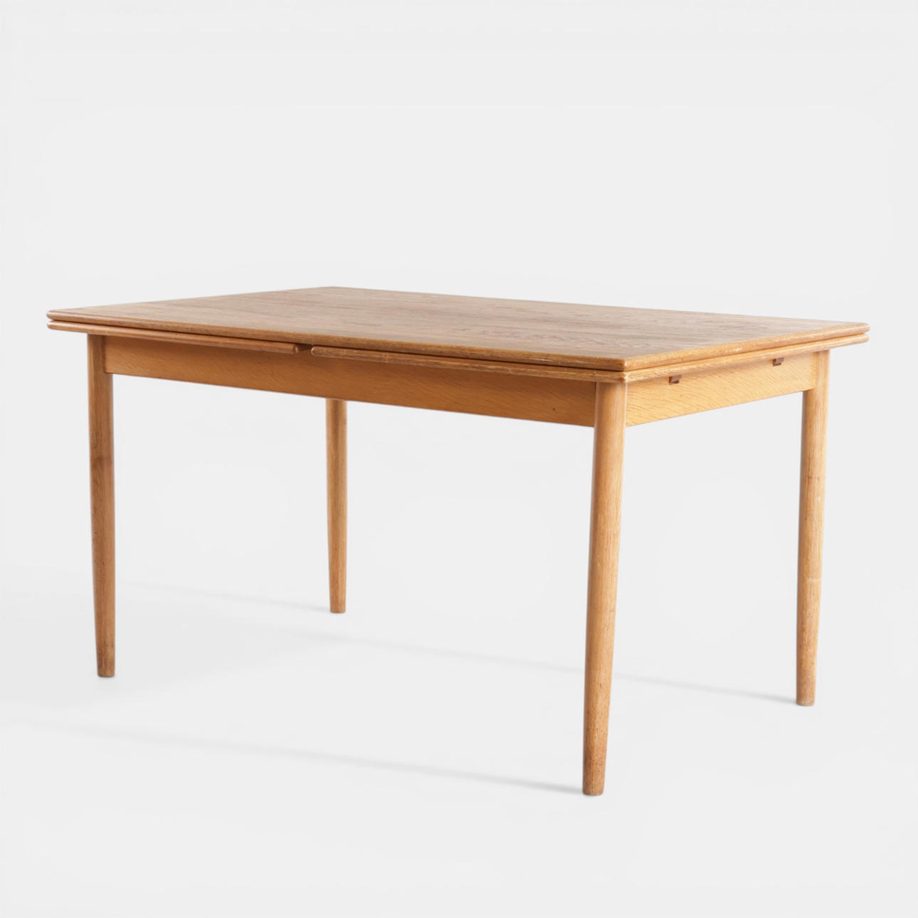 Rectangular dining table in oak, top with Dutch pull-out leaves, round tapered legs. Denmark, 1960s-70s.