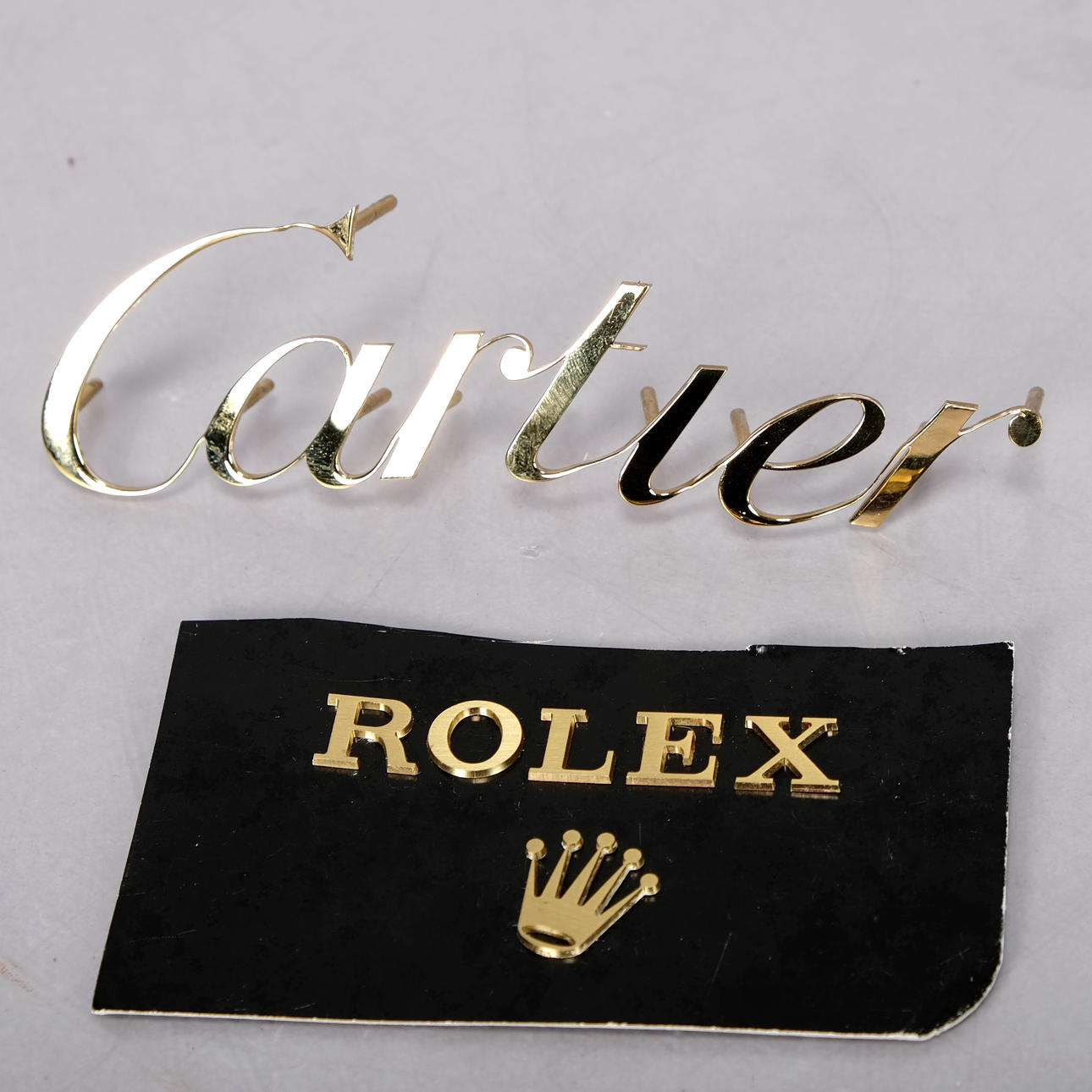 CARTIER OCH ROLEX, emblem, mässing, (2 delar.