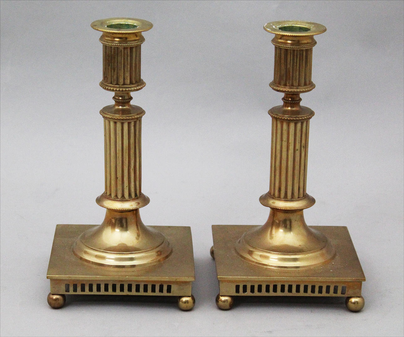 MÄSSINGSLJUSSTAKAR (2). Gustaviansk stil. Kannelerade skaft. Kvadratiska fotplattor, med gallerkant och kulfötter.