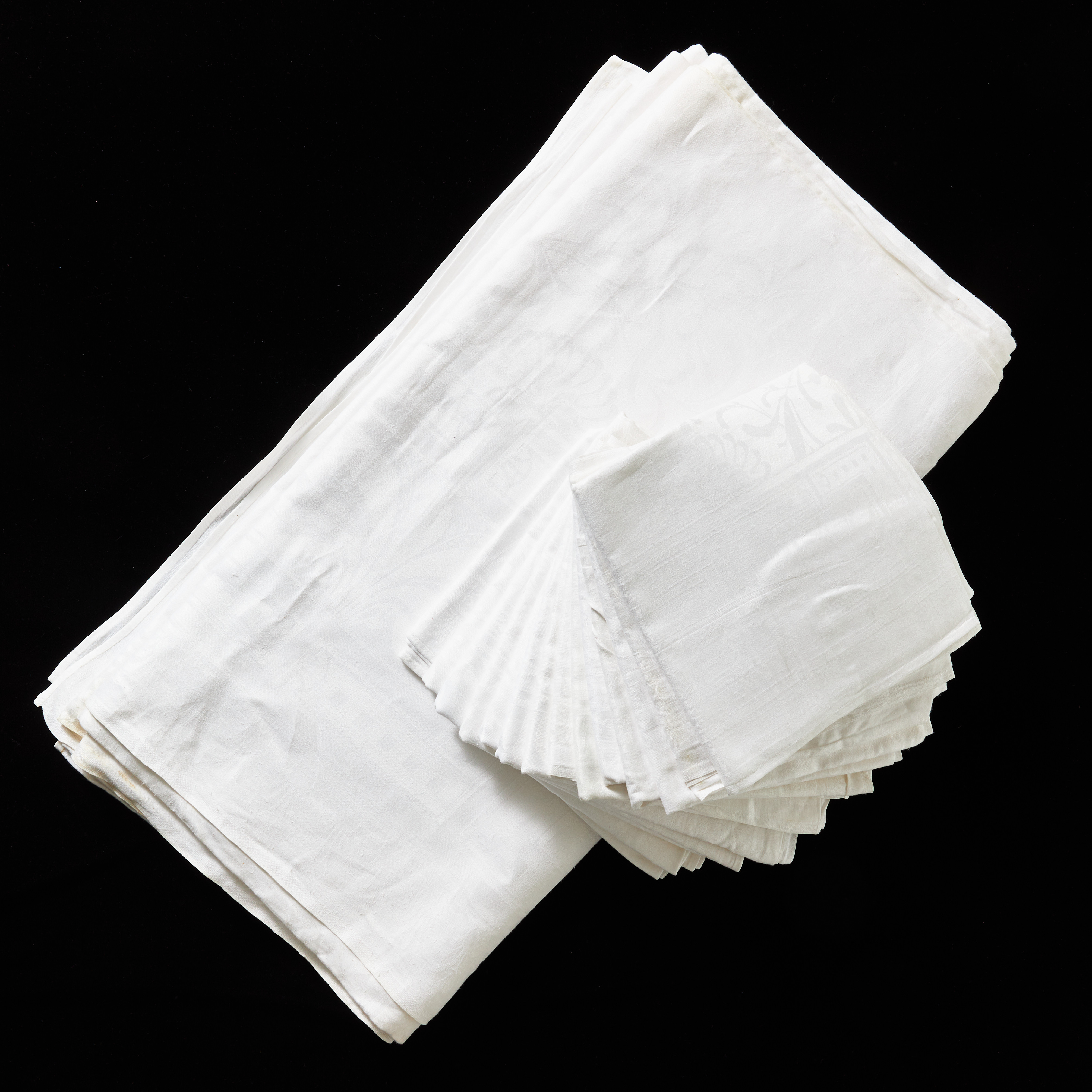 BORDSDUK med 14 SERVETTER, linnedamast, omkring år 1900, jugend, spegel med dekor av mistelblad, bred bård med kvadratiska kartuscher med stiliserade växter, ytterst med palmettbård, broderat monogram (S [...?]).